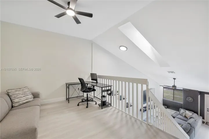 Open loft area featuring vaulted ceilings, a skylight, wood-finish flooring, and a ceiling fan with integrated lighting