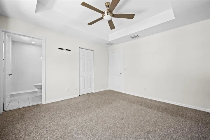 Additional view of the primary suite highlighting the tray ceiling, generous floor space, and access to the​​‌​​​​‌​​‌‌​‌‌​​​‌‌​‌​‌​‌​​​‌​​ bathroom.
