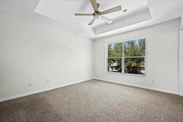 Spacious primary suite with a tray ceiling, ceiling fan, and natural light.