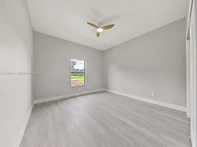 Neutral-toned interior space featuring wood-finish flooring, a contemporary three-blade ceiling fan with integrated lighting, and a single-pane window