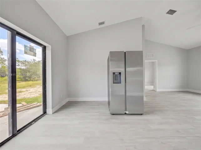 Vaulted ceilings, expansive glass sliding doors, wood-finish flooring, and a stainless steel side-by-side refrigerator