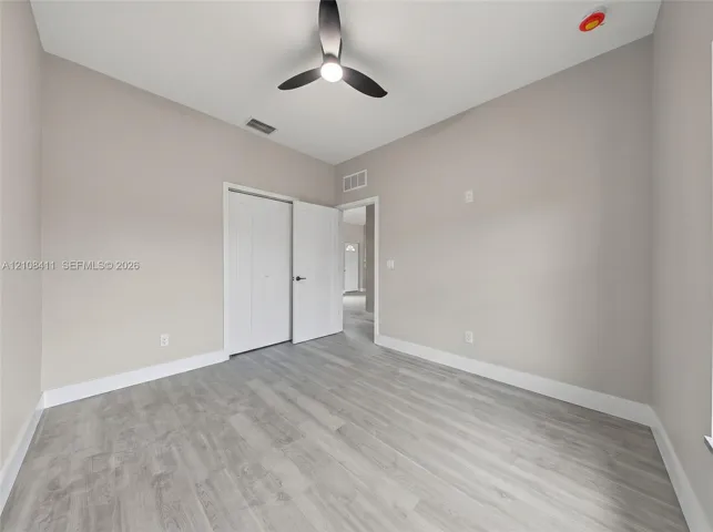 Neutral-toned interior featuring wood-finish flooring, a modern three-blade ceiling fan with integrated lighting, and a dual-panel closet door