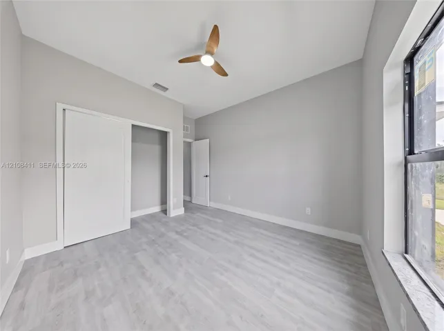 Neutral-toned interior featuring wood-finish flooring, a contemporary three-blade ceiling fan with integrated lighting, sliding closet doors, and a large window with a stone-finish sill