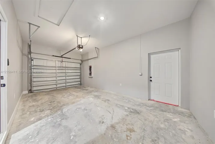 Finished garage featuring smooth-finish interior walls, a recessed ceiling light, an overhead garage door mechanism, and an exterior-access door
