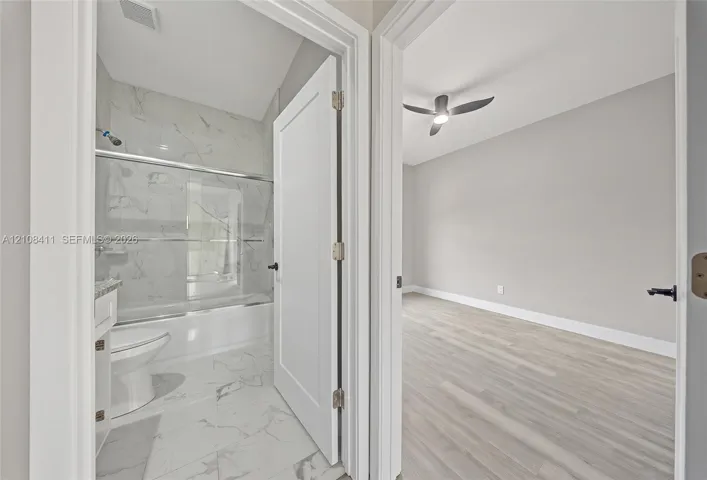 Full bathroom with a tub-shower combination featuring tile surround, and an interior room with wood-finish flooring and a ceiling fan