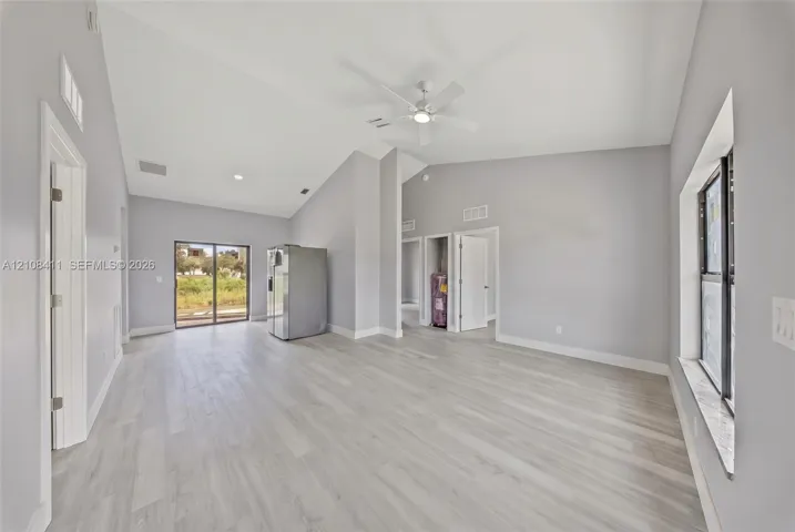Open-concept interior featuring vaulted ceilings, wood-finish flooring, a ceiling fan, and sliding glass doors