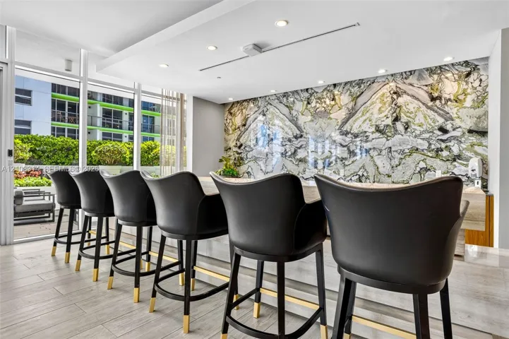 Stone accent wall with book-matched detailing, expansive floor-to-ceiling glass windows, recessed ceiling lighting, and neutral-toned tile flooring