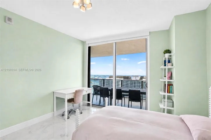 Room with large glass sliding doors, polished stone-finish flooring, and built-in white shelving, providing access to a private balcony