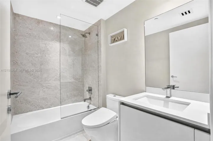 Bathroom featuring a vanity with a white countertop and integrated sink, frameless glass shower enclosure, stone-finish tile surround, and large wall-mounted mirror
