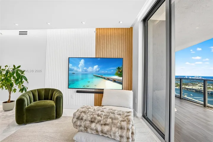 Custom accent wall featuring vertical wood-slat and fluted detailing, recessed ceiling lighting, and expansive floor-to-ceiling sliding glass doors leading to a private balcony