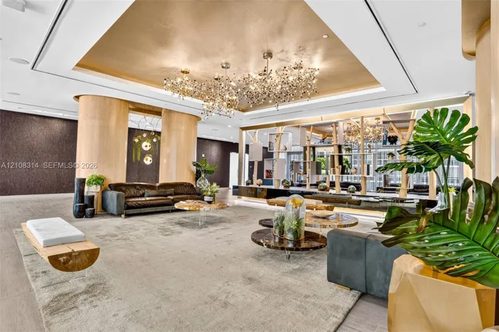 Metallic tray ceiling, large-scale multi-bulb crystal chandeliers, curved light-wood structural columns, integrated architectural shelving, and recessed lighting
