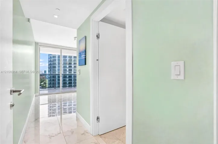 Hallway featuring large-format tile flooring, light-toned wall finishes, and floor-to-ceiling glass sliding doors