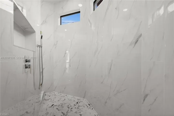 Walk-in shower featuring large-format stone-pattern wall tile, recessed built-in shelving, a handheld shower fixture, and clerestory windows