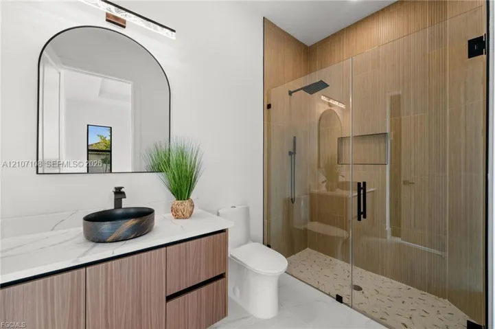 Floating vanity with a stone-finish countertop, arched wall mirror, vessel sink with matte black hardware, and a walk-in shower featuring tile walls, a built-in recessed niche, and a glass enclosure
