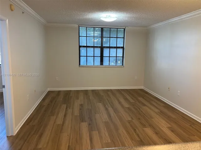 Room interior featuring wood-finish flooring, neutral wall tones, multi-pane window with horizontal blinds, and crown molding
