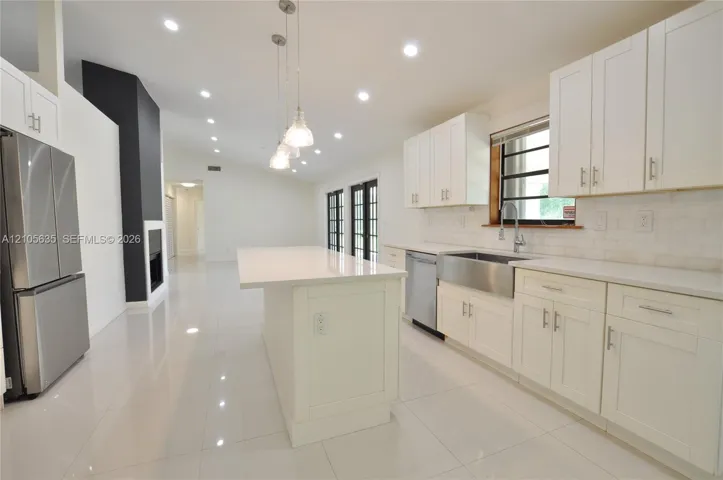 Kitchen featuring white shaker-style cabinetry, quartz countertops, a stainless steel apron-front sink, an island with pendant lighting, and polished tile flooring