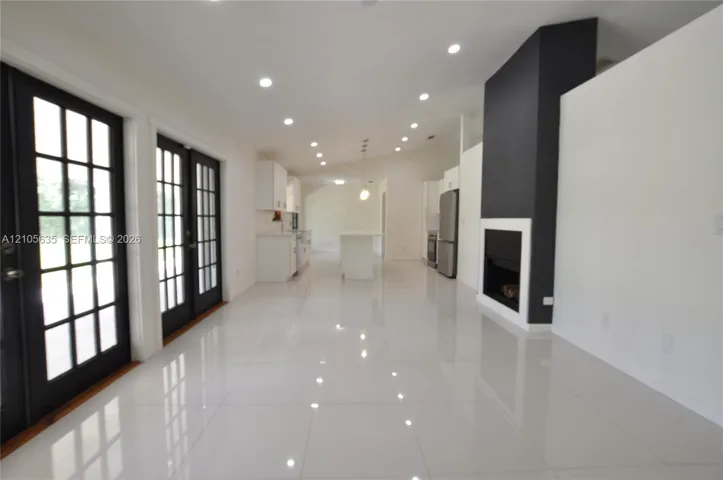 Open interior featuring white tile flooring, recessed lighting, double French doors with black frames, and a floor-to-ceiling fireplace with a contrast hearth