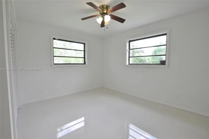 Neutral interior featuring large-format tile flooring, dual windows, a ceiling fan with integrated lighting, and louvered closet doors