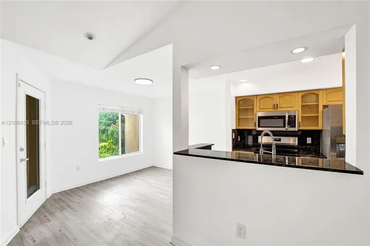 Kitchen featuring wood-finish cabinetry, stone-surface counters, and built-in stainless steel appliances, accented by wood-finish flooring, vaulted ceilings, and recessed lighting