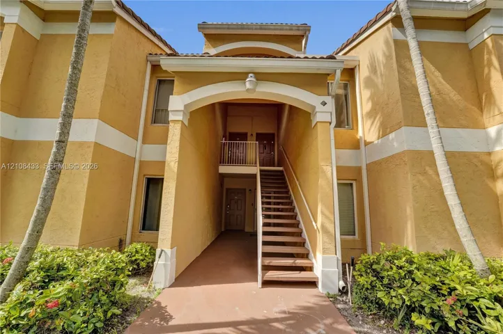 Stucco exterior featuring an arched entryway, decorative trim, tiled roofline, and exterior staircase