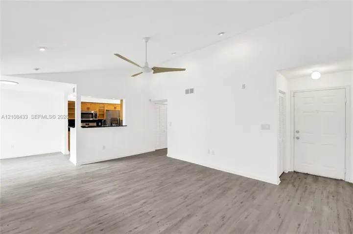 Vaulted ceilings, wood-finish flooring, ceiling fan with light fixture, recessed lighting, and pass-through counter opening to kitchen