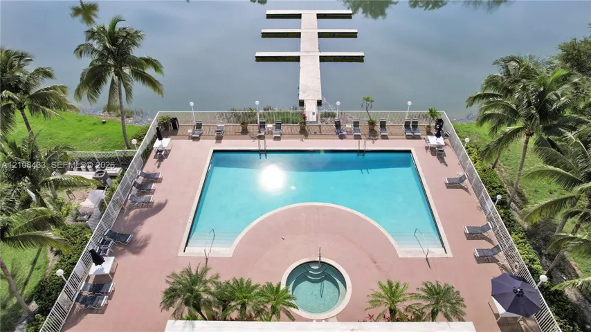 Waterfront exterior featuring a swimming pool, integrated spa, concrete boat dock, and perimeter fencing