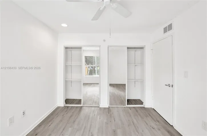Wood-finish flooring, dual closets with sliding mirrored doors, built-in shelving, and a ceiling fan