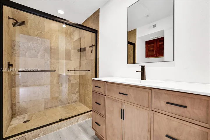 Walk-in shower with stone tile surround, frameless glass enclosure, and matte black fixtures