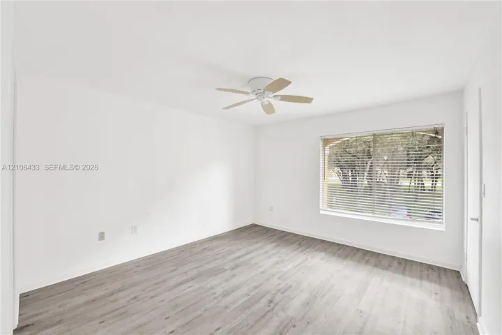 Neutral-toned walls, wood-finish flooring, ceiling-mounted fan, and a large window with horizontal blinds