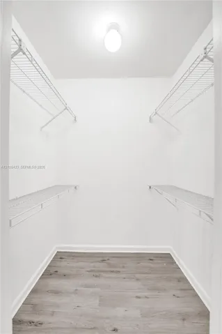 Walk-in closet featuring dual-level white wire shelving, flush-mount dome lighting, and wood-finish flooring