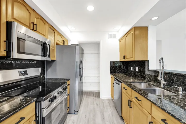 Kitchen featuring natural finish cabinetry, dark stone countertops, stainless steel appliances, a pull-down kitchen faucet, and wood-finish flooring