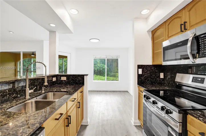 Kitchen featuring medium-tone wood cabinetry, dark stone countertops, stainless steel appliances, a dual-basin undermount sink, and wood-finish flooring