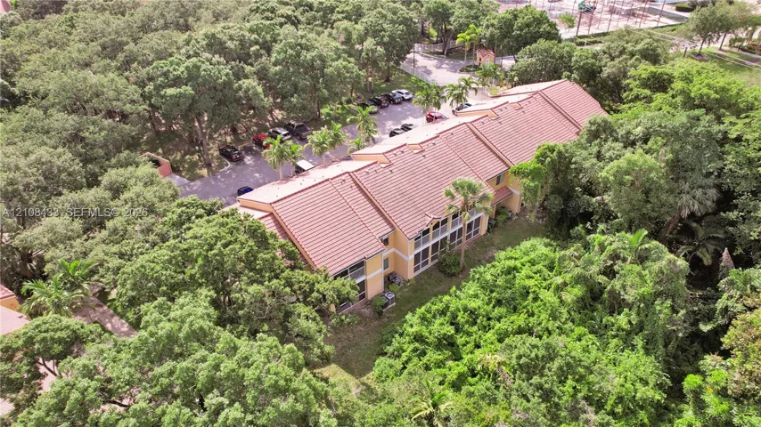 Multi-story residential building featuring a tile roof, light-toned exterior finish, screened balconies, and extensive surrounding tree canopy