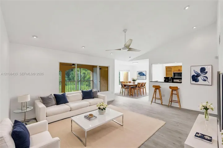 Living area featuring vaulted ceilings, recessed lighting, wood-finish flooring, a ceiling fan, and a pass-through opening to the kitchen