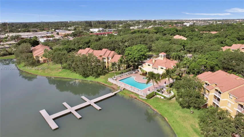 Aerial perspective featuring multi-story structures with tile roofing, an inground swimming pool, and a private dock extending into the lakefront