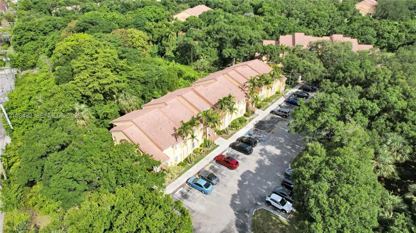 Multi-story building featuring a tile roof, exterior stucco siding, and designated asphalt surface parking, situated among mature trees and dense vegetation