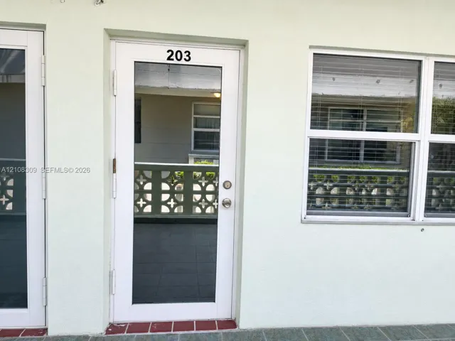 White-framed glass entry door, multi-pane window with integrated blinds, and decorative concrete screen wall