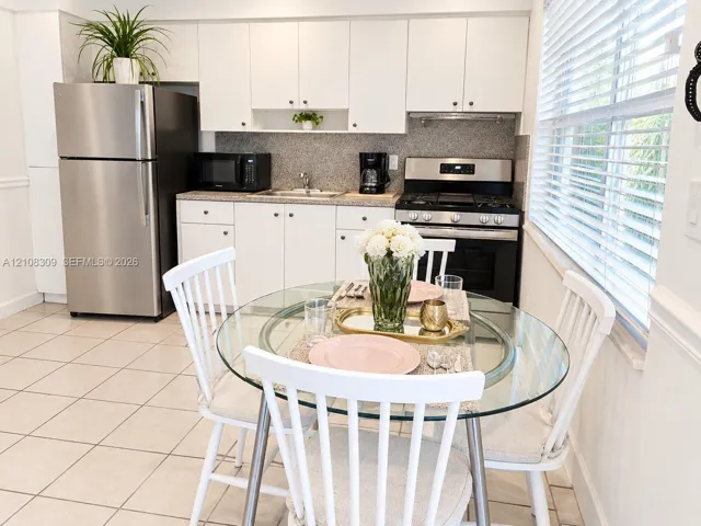 Kitchen featuring white cabinetry, stainless steel appliances, neutral stone-finish countertops, tiled flooring, and horizontal window blinds