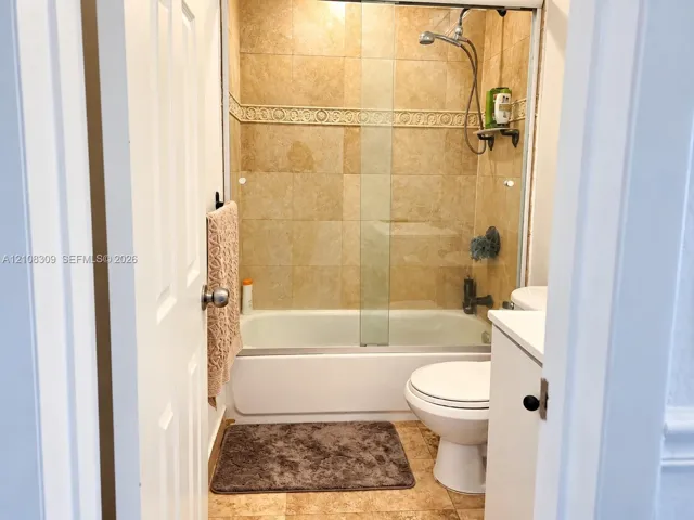 Full bathroom featuring a tub-shower combination with a glass door, natural stone-style wall tile, decorative tile inlay, and stone-style flooring