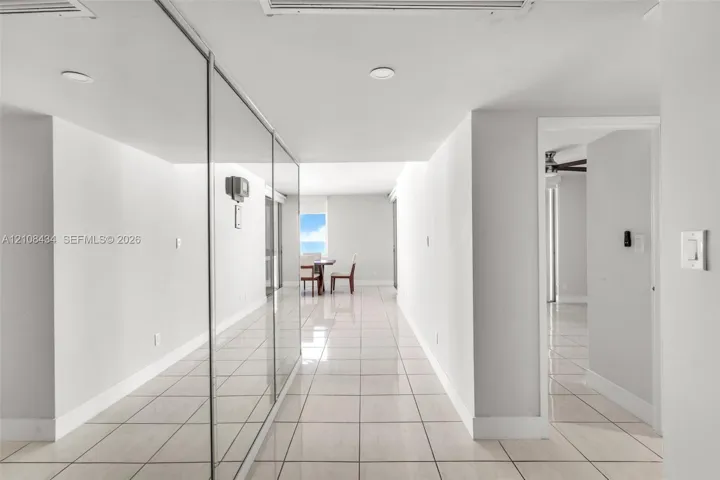 Interior hallway featuring light-toned tile flooring, floor-to-ceiling mirrored wall panels, and recessed lighting