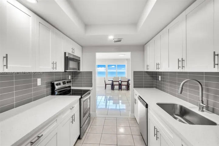 Kitchen featuring white shaker-style cabinetry, solid-surface countertops, horizontal gray tile backsplash, stainless steel appliances, and large-format tile flooring