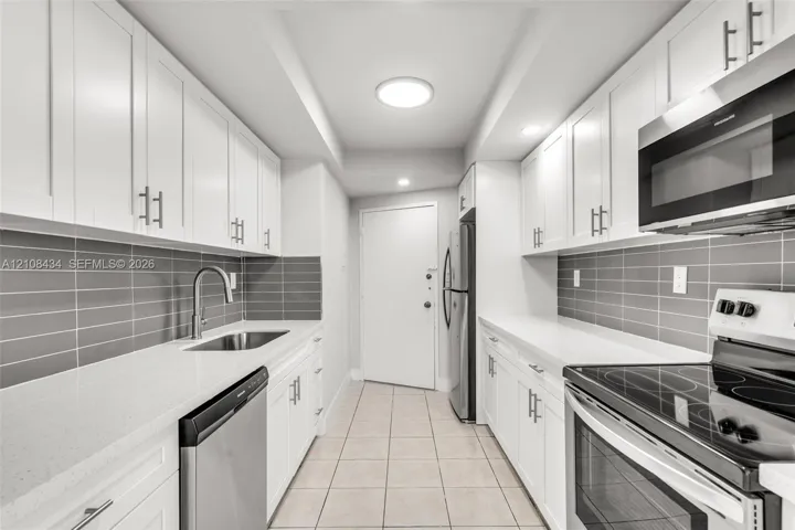 Kitchen featuring white shaker-style cabinetry, white countertops, gray subway tile backsplash, stainless steel appliances, and tile flooring