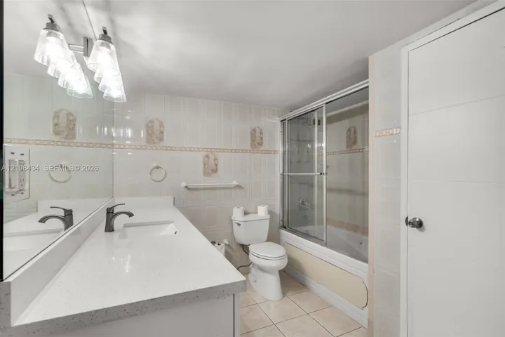 Bathroom featuring a quartz-topped vanity with an integrated basin, ceramic tile flooring, full-width wall mirror, and a tub-shower combination enclosed by sliding glass doors