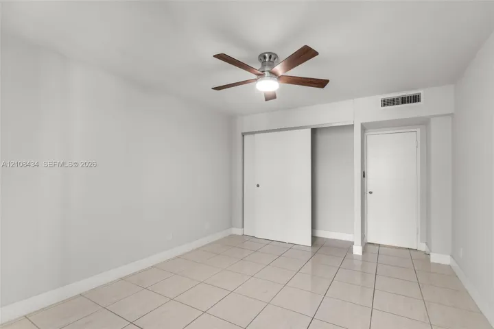 Neutral-toned room featuring large-format tile flooring, a multi-blade ceiling fan with integrated lighting, a sliding-door closet, and a contemporary flat-panel door