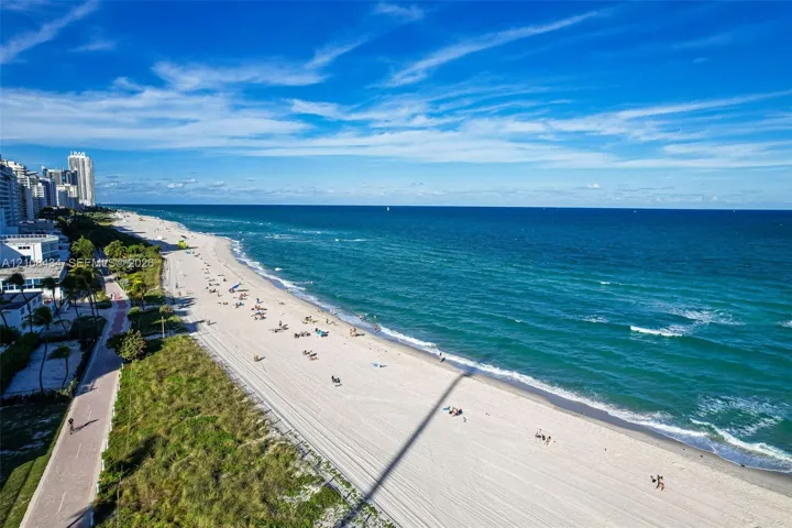 Direct oceanfront location featuring a sandy beach, pedestrian walkway, and coastal vegetation