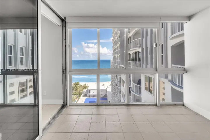 Enclosed balcony featuring tile flooring, floor-to-ceiling windows, and sliding glass panel doors, showcasing ocean and coastline scenery
