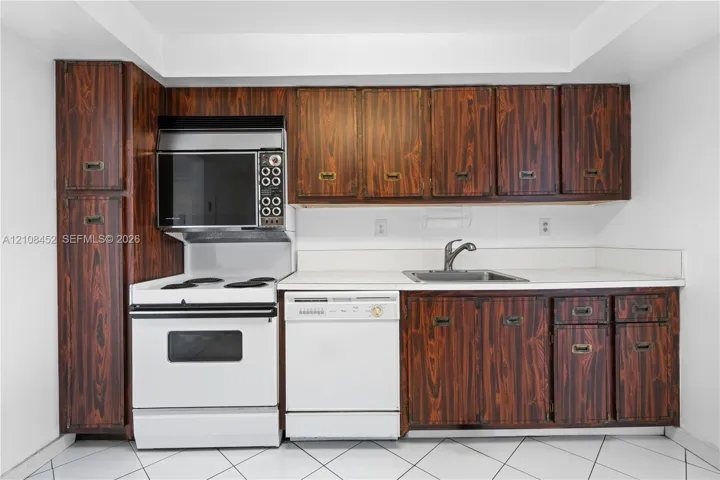 Kitchen featuring wood-grain cabinetry, solid surface countertops, white electric range with built-in microwave, integrated dishwasher, and stainless steel sink
