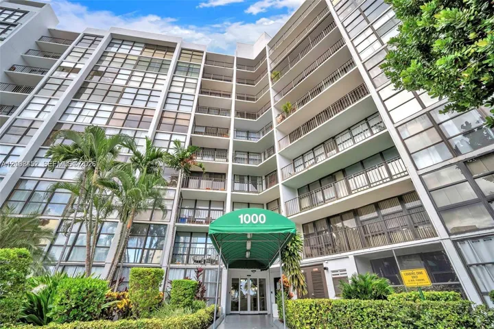 High-rise exterior featuring extensive glass paneling, a concrete facade, private balconies, and an arched green entryway canopy