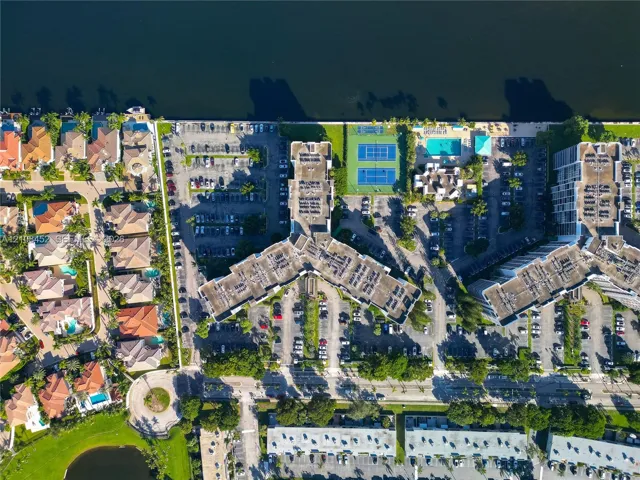 Aerial perspective of a multi-unit residential property featuring waterfront access, two tennis courts, and a swimming pool
