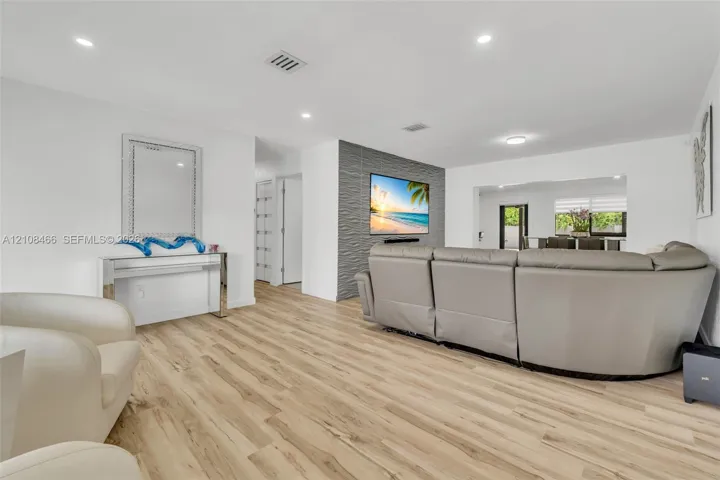 Living area featuring wood-finish flooring, recessed lighting, and a grey textured accent wall